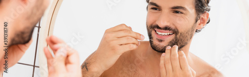 Smiling man holding dental floss near mirror on blurred foreground in bathroom, banner