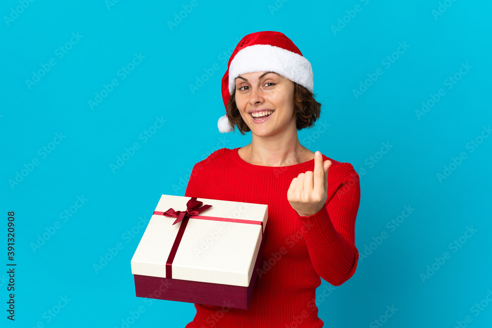 English girl with christmas hat holding a present isolated on blue background making money gesture English girl with christmas hat holding a present isolated on blue background making money gesture