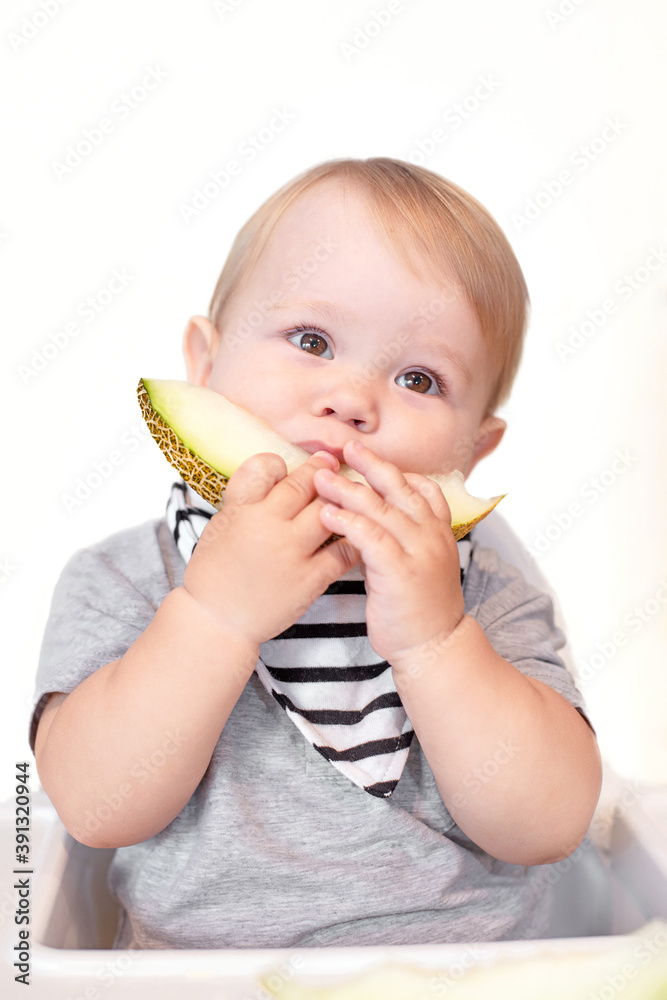 the child sits on a high chair and eats a melon, complementary foods for a 1 year old baby, teething teeth, the baby's first feeding, a hypoallergenic diet the child sits on a high chair and eats a melon, complementary foods for a 1 year old baby, teething teeth, the baby's first feeding, a hypoallergenic diet