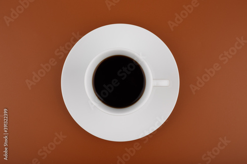 Top view of white coffee cup on plate on brown background
