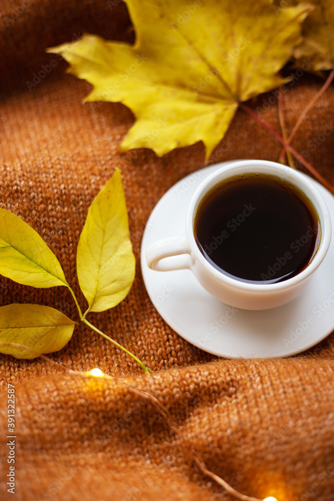 A cup of coffee on an orange sweater, yellow leaves, lights in the background. Warm autumn. A cup of coffee on an orange sweater, yellow leaves, lights in the background. Warm autumn.