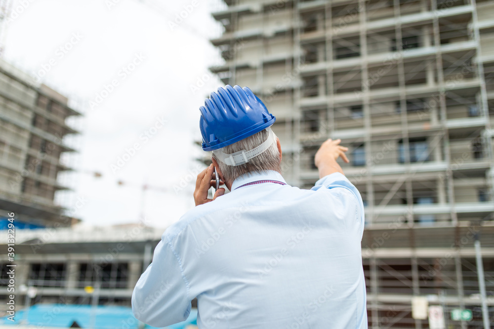 Architect manager talking on the cellphone and pointing his finger to a construction site