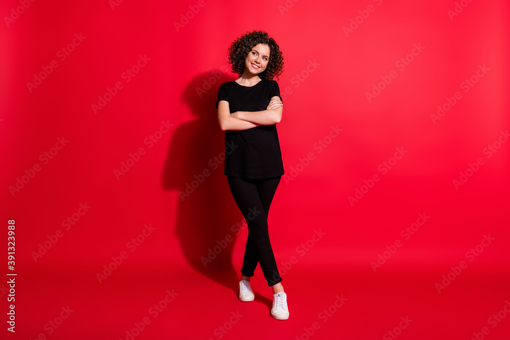 Full body photo of curious interested girl smile crossed hands curly hair isolated over red color background Full body photo of curious interested girl smile crossed hands curly hair isolated over red color background