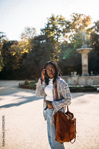 Portrait of a pretty black woman in stylish casual shirt with brown bag walks in an autumnal park