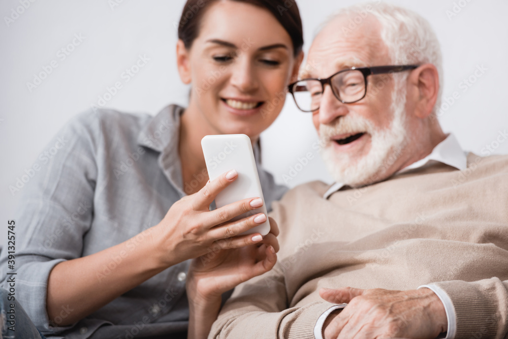 smiling woman showing mobile phone to cheerful aged father on blurred background smiling woman showing mobile phone to cheerful aged father on blurred background