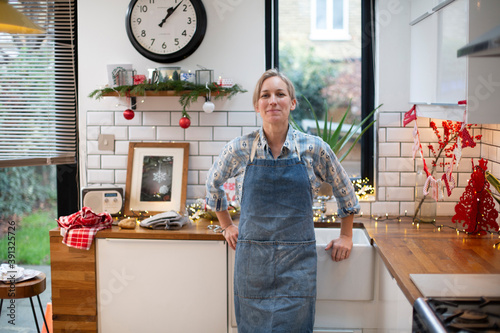 Blond woman wearing blue apron standing in kitchen, smiling at camera. photo