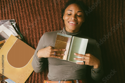 Smiling black woman lying on floor holding book next to stack of vinyl records photo