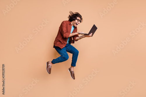 Photo portrait full body view of screaming guy jumping up with laptop in hands isolated on pastel beige colored background