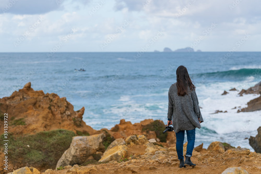 Caucasian woman looking at an island on the ocean from a cliff in Peniche, Portugal