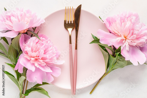 Fototapeta Naklejka Na Ścianę i Meble -  Pink peony flowers and a plate with cutlery on the table. Top view. Flat lay