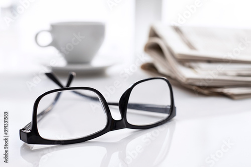 Newspapers and coffee cup, with reading glasses. 