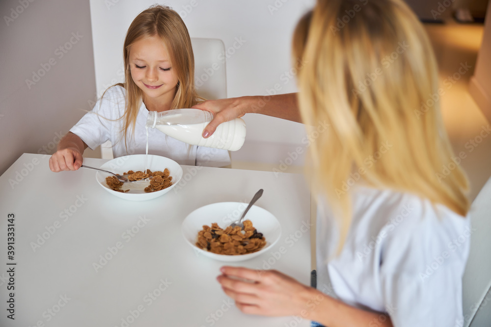 Mother pouring milk for daughter breakfast in the morning Mother pouring milk for daughter breakfast in the morning