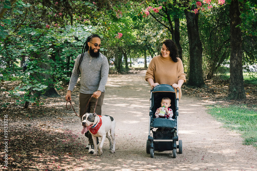 Latinx couple walking in park with their baby in stoller and pet dog photo