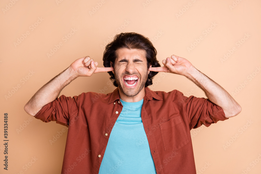 Portrait of nice worried fury guy closing ears grimacing dislike isolated over beige pastel color background Portrait of nice worried fury guy closing ears grimacing dislike isolated over beige pastel color background