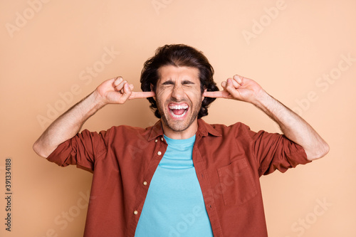 Portrait of nice worried fury guy closing ears grimacing dislike isolated over beige pastel color background