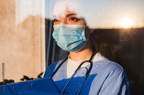 Foto Young sad female caucasian UK US NHS EMS doctor carer looking through ICU window