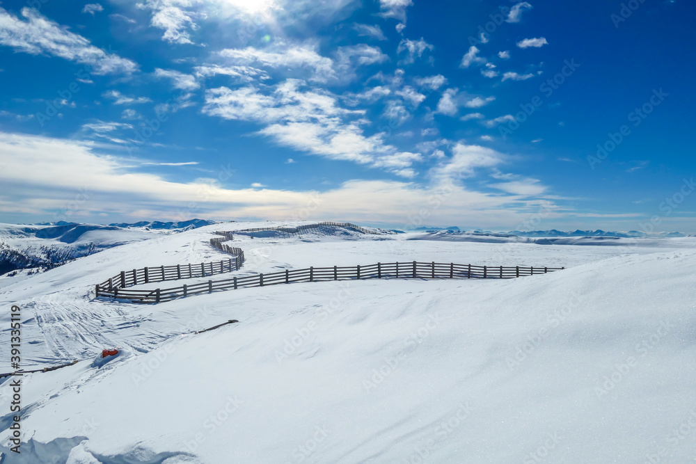 Panoramic view on snow capped Alps in Austria, seen from Katschberg Ski Resort. There is a fence going through the middle of the slope. The slopes are covered with fresh, powder snow. Winter landscape