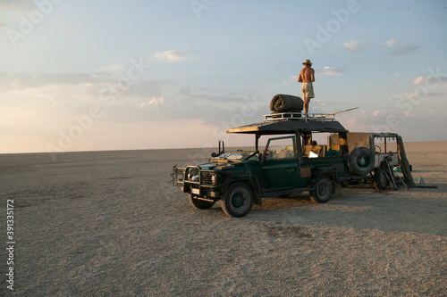Man standing on top of 4x4 parked on the Makadikadi Salt Pans in Botswana. photo