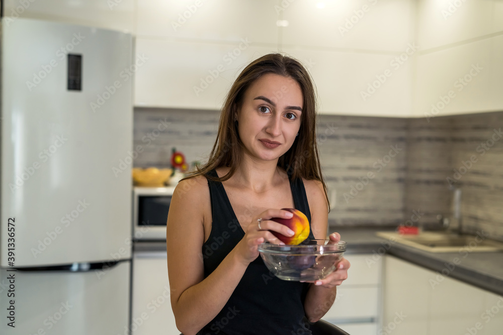 portrait of young woman standing near desk with fresh fruit in the kitchen