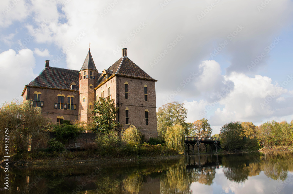 Dutch medieval castle in autumn landscape with moat and fall trees. Castle reflection in water. Dramatic afternoon light. Travel destination gelderland, the netherlands. Heritage buildings. 