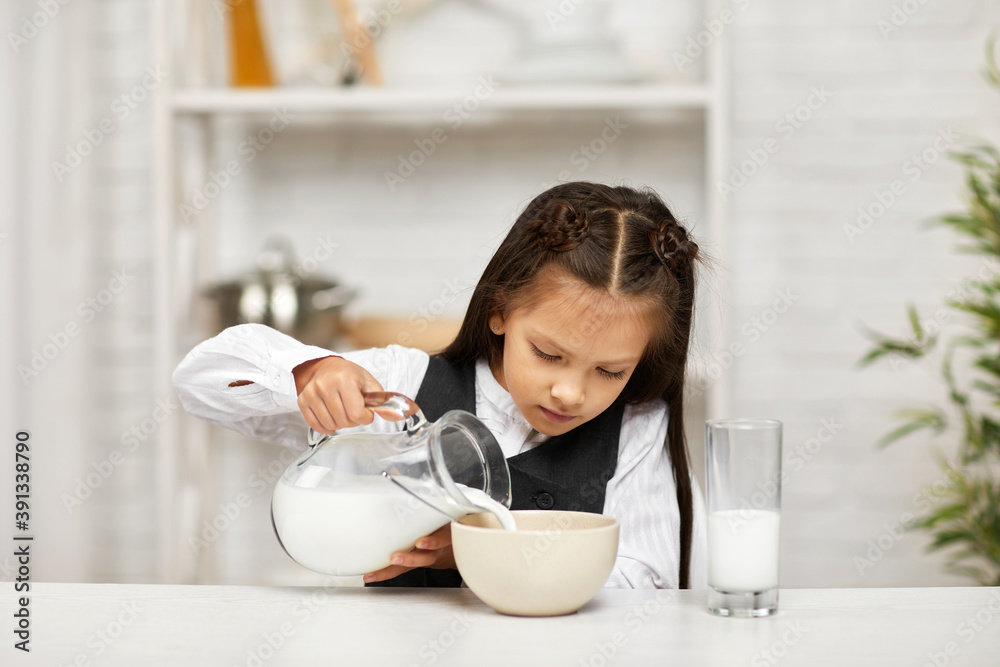 little girl eating breakfast: cereal with the milk. child in school uniform pours milk into a bowl of cereal in the kitchen. healthy breakfast little girl eating breakfast: cereal with the milk. child in school uniform pours milk into a bowl of cereal in the kitchen. healthy breakfast