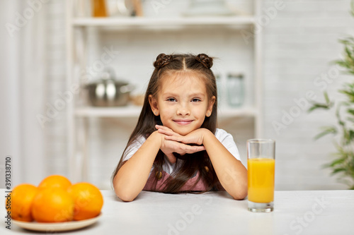 happy little child girl with oranges and juice in the kitchen. healthy food