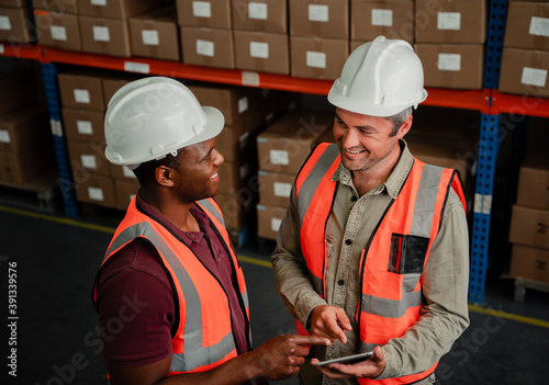 Two colleagues smiling while discussing business plans holding digital tablet standing in warehouse  photo