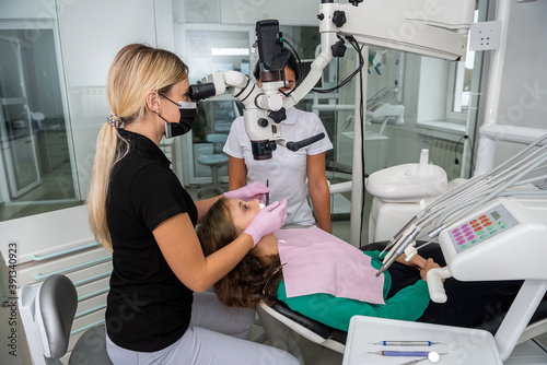 Female dentist checking up patient teeth using microscope  and instruments at modern clinic.