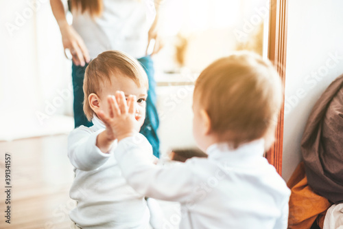 A little child looks in the mirror with his palm on the glass