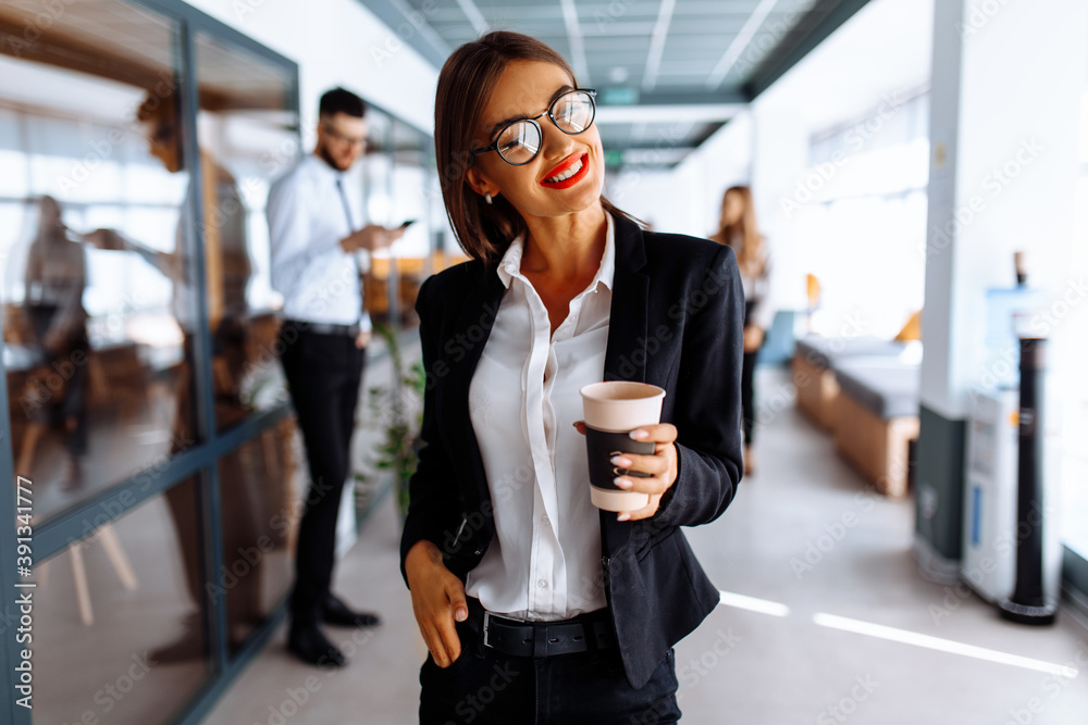 Business attractive young woman walking down the corridor in the office drinking coffee during the break