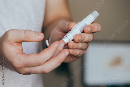 Medicine  diabetes  glycemia  healthcare and people concept - close up of a man s hands using a lancet on his finger to check blood glucose meter with copy space for text