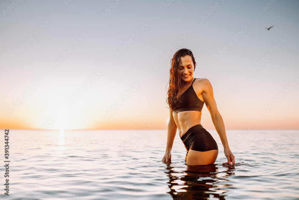 Young sporty woman in calm sea at sunset in black sportswear. Space for message.