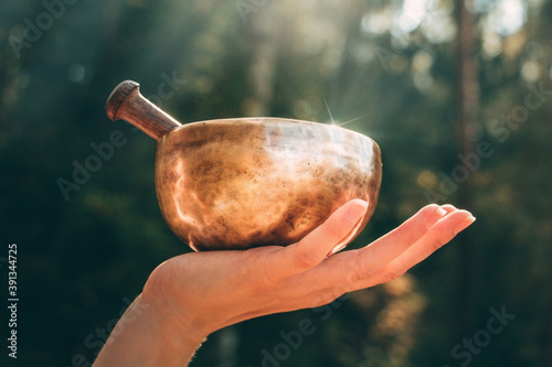 The hand holding a golden singing bowl. Tibetan bowl in the rays of the sun. Illumination and light. Qi energy. Gratitude to the world.