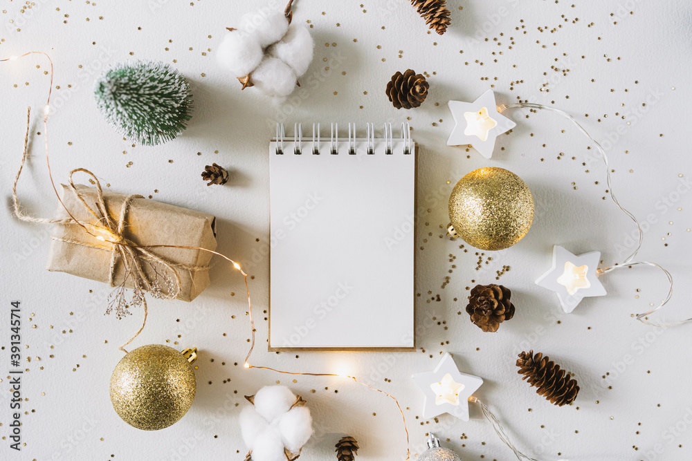 Christmas festive decorations and notebook. With wish list and 2021 goals concept. Notebook mock up, gift, and coton branch with shiny golden balls.New year flat lay, top view, copy space.. - obrazy, fototapety, plakaty 