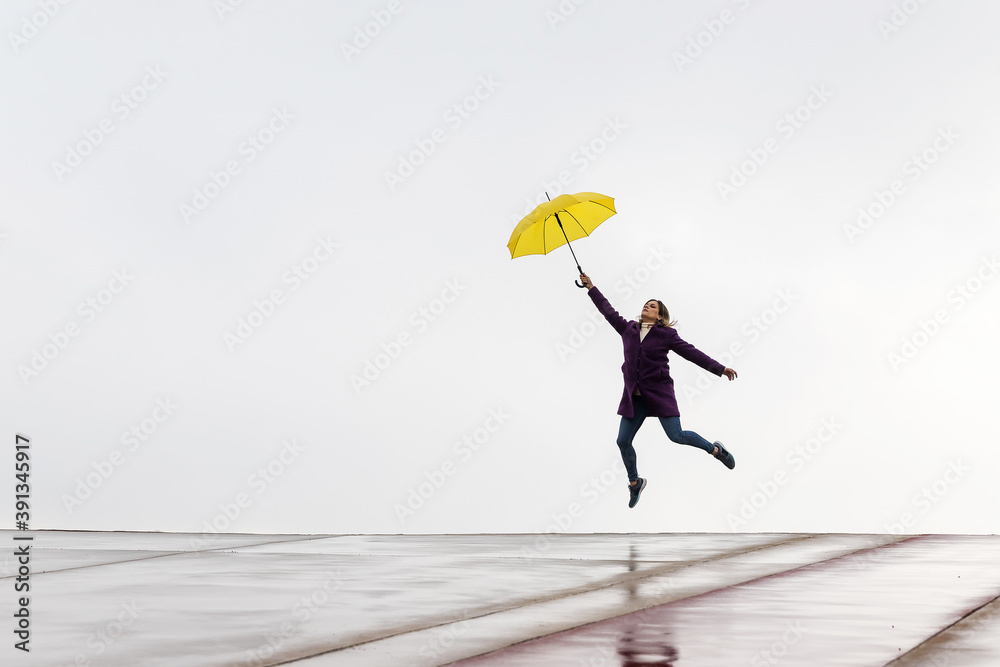 Woman jumping on the horizon with a yellow umbrella on a rainy day