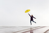 Woman jumping on the horizon with a yellow umbrella on a rainy day