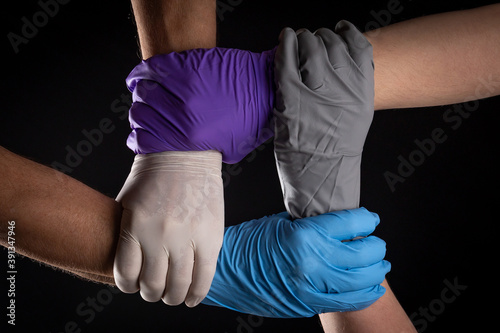 Men in latex gloves of different colors, holding hands in a circle on a black background.