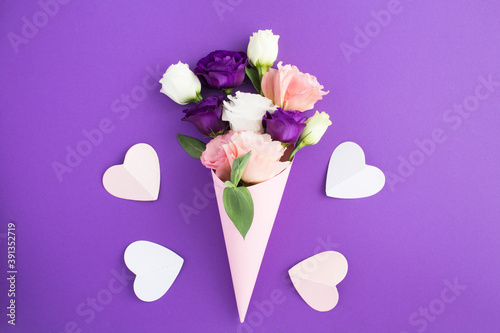 White, pink and violet flowers in a paper pink cone and pink hearts on the violet background closeup