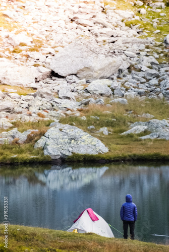 The tourist is standing near the tent. Lake in the Carpathian mountains. Girl in a warm jacket.