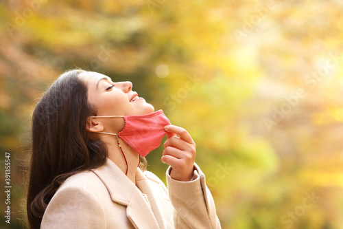 Woman taking off mask breathing fresh air in autumn