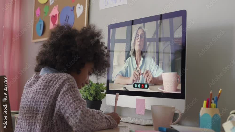 Smart small african school child girl online learning with online remote teacher or web tutor studying at home on computer taking notes. Tutoring, homeschool social distance virtual education concept.