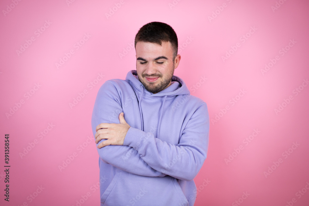 Young handsome man wearing casual sweatshirt over isolated pink background hugging oneself happy and positive, smiling confident Young handsome man wearing casual sweatshirt over isolated pink background hugging oneself happy and positive, smiling confident