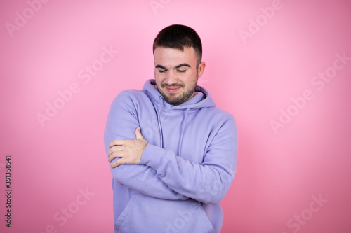 Young handsome man wearing casual sweatshirt over isolated pink background hugging oneself happy and positive, smiling confident