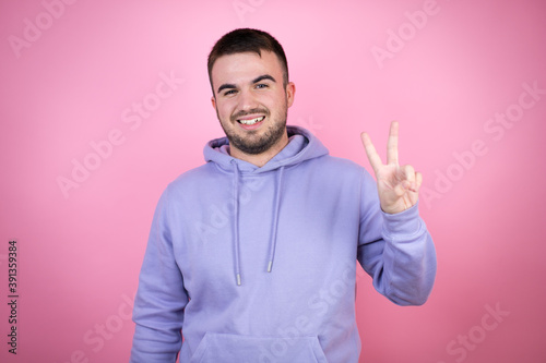 Young handsome man wearing casual sweatshirt over isolated pink background showing and pointing up with fingers number two while smiling confident and happy