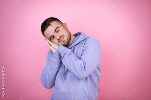 Young handsome man wearing casual sweatshirt over isolated pink background sleeping tired dreaming and posing with hands together while smiling with closed eyes. © Irene