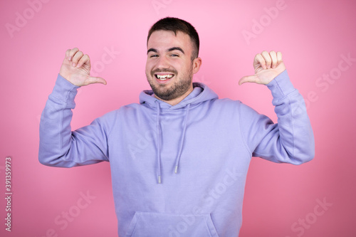 Young handsome man wearing casual sweatshirt over isolated pink background looking confident with smile on face, pointing oneself with fingers proud and happy.