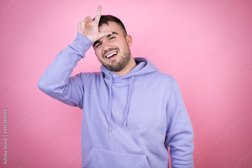 Young handsome man wearing casual sweatshirt over isolated pink background making fun of people with fingers on forehead doing loser gesture mocking and insulting. Young handsome man wearing casual sweatshirt over isolated pink background making fun of people with fingers on forehead doing loser gesture mocking and insulting.
