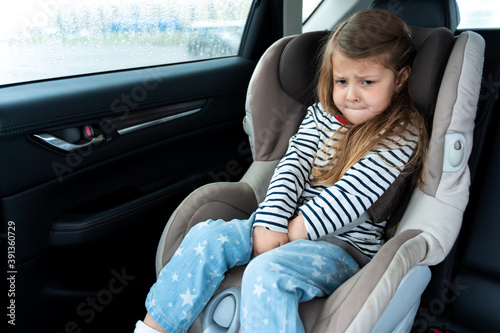 Little girl is driving in car. Kid child wants to go to toilet, pee and endures. Traveling, riding on road in safe baby seats with child belts. Fun family trip, activity with parents