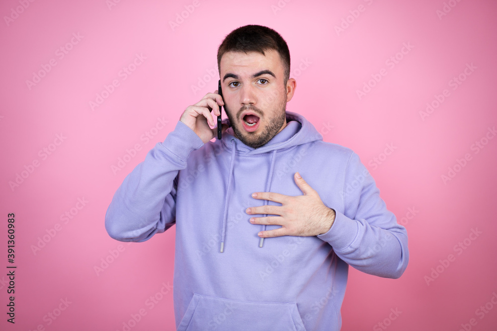 Young handsome man wearing casual sweatshirt over isolated pink background talking on the phone with a worried expression Young handsome man wearing casual sweatshirt over isolated pink background talking on the phone with a worried expression