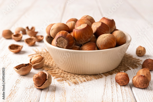 Unpshelled hazelnuts in a beige ceramic bowl on a white wood table. Healthy vegetarian eating, antioxidant and protein source. Ketogenic and raw food diets ingredient.